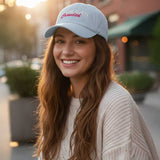 Woman wearing a light blue cap with "make heaven crowded" text, smiling outdoors.