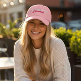 Woman wearing a pink cap with text "Make heaven crowded", sitting outdoors.